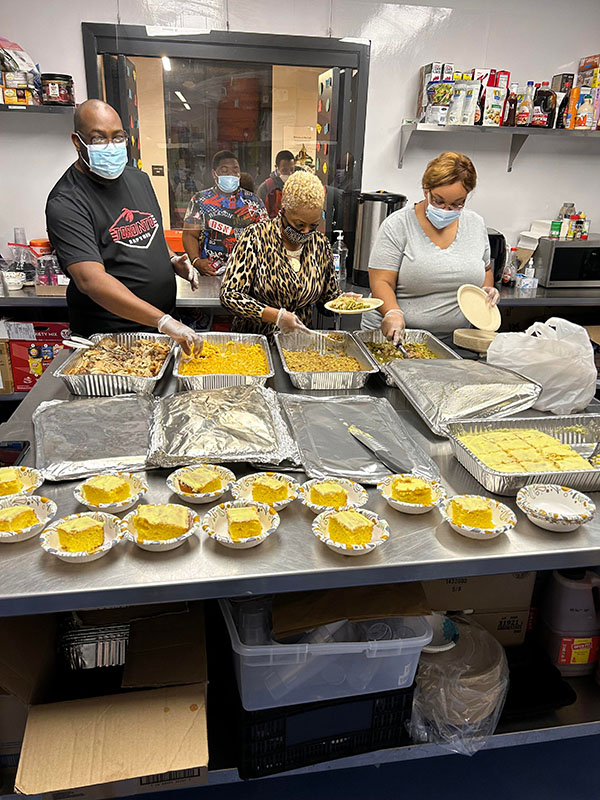 Three people standing in a kitchen preparing food.